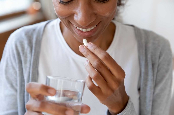 Close up happy young african american young woman taking daily dose of complex healthcare skin, hair and nails omega vitamins drinking glass of fresh pure water, immunity improvement concept.