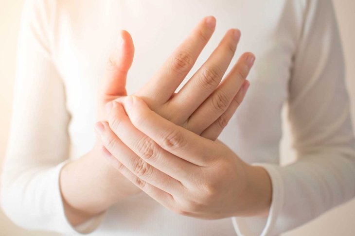 Young female in white t-shirt suffering from pain in hands and massaging her painful hands. Causes of hurt include carpal tunnel syndrome, fractures, arthritis or trigger finger. Health care concept.