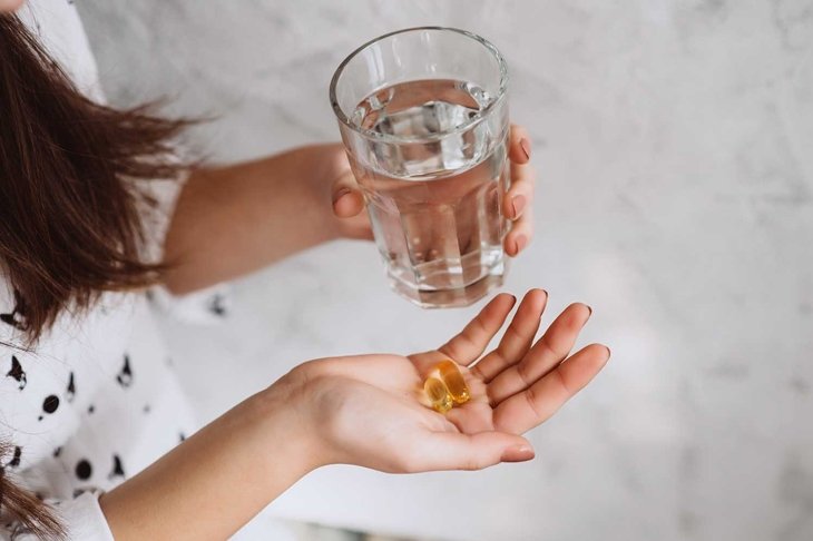 Diet. Nutrition. Girl\'s hands with pills with cod liver omega-3 oil and a glass of fresh water. The concept of a healthy diet and lifestyle. Vitamin D, E, fish oil capsules.
