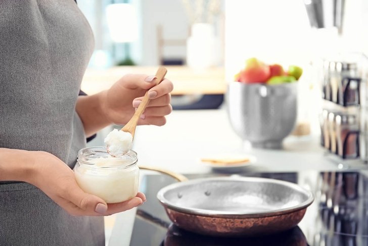 Woman putting coconut oil on frying pan in kitchen, closeup