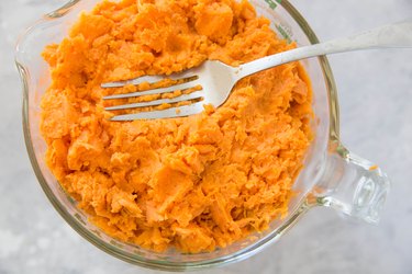 Measuring cup with mashed sweet potato and a fork