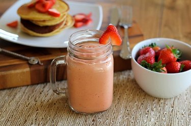 A healthy strawberry smoothie served with fresh strawberries and pancakes.
