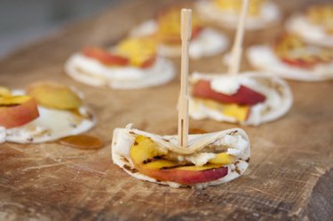 Mini-tortillas with ricotta cheese and grilled peaches atop wood cutting board.