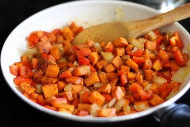 Sauteed onion, sweet potato and bell pepper in a skillet.
