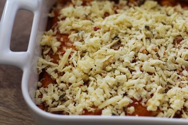 Casserole dish of uncooked enchiladas with grated cheese.