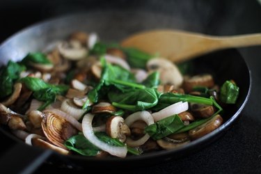 Sauteed onion, mushrooms and spinach in a frying pan.