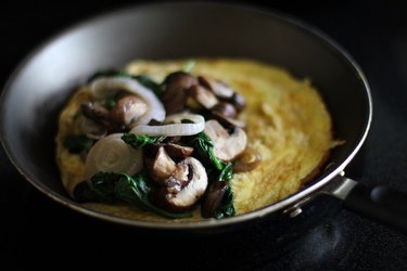 Sauteed onions, mushrooms and spinach placed on one half of the cooked eggs in a skillet.